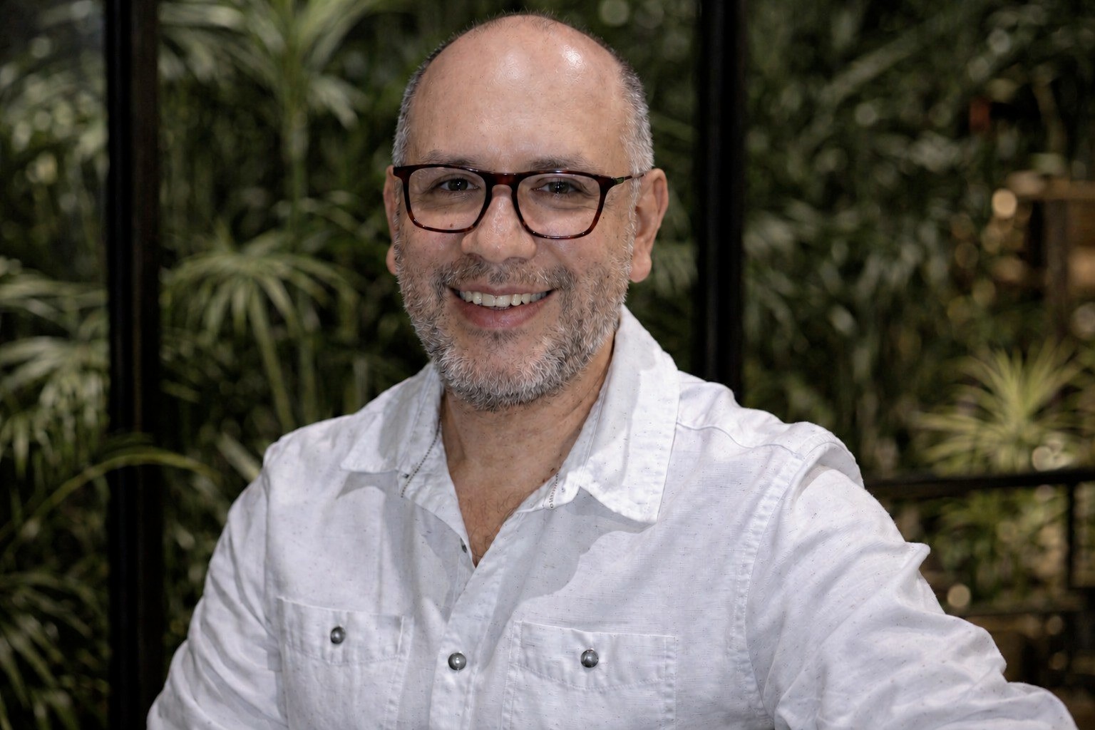 Hubert Ronald smiling, wearing glasses and a white shirt.